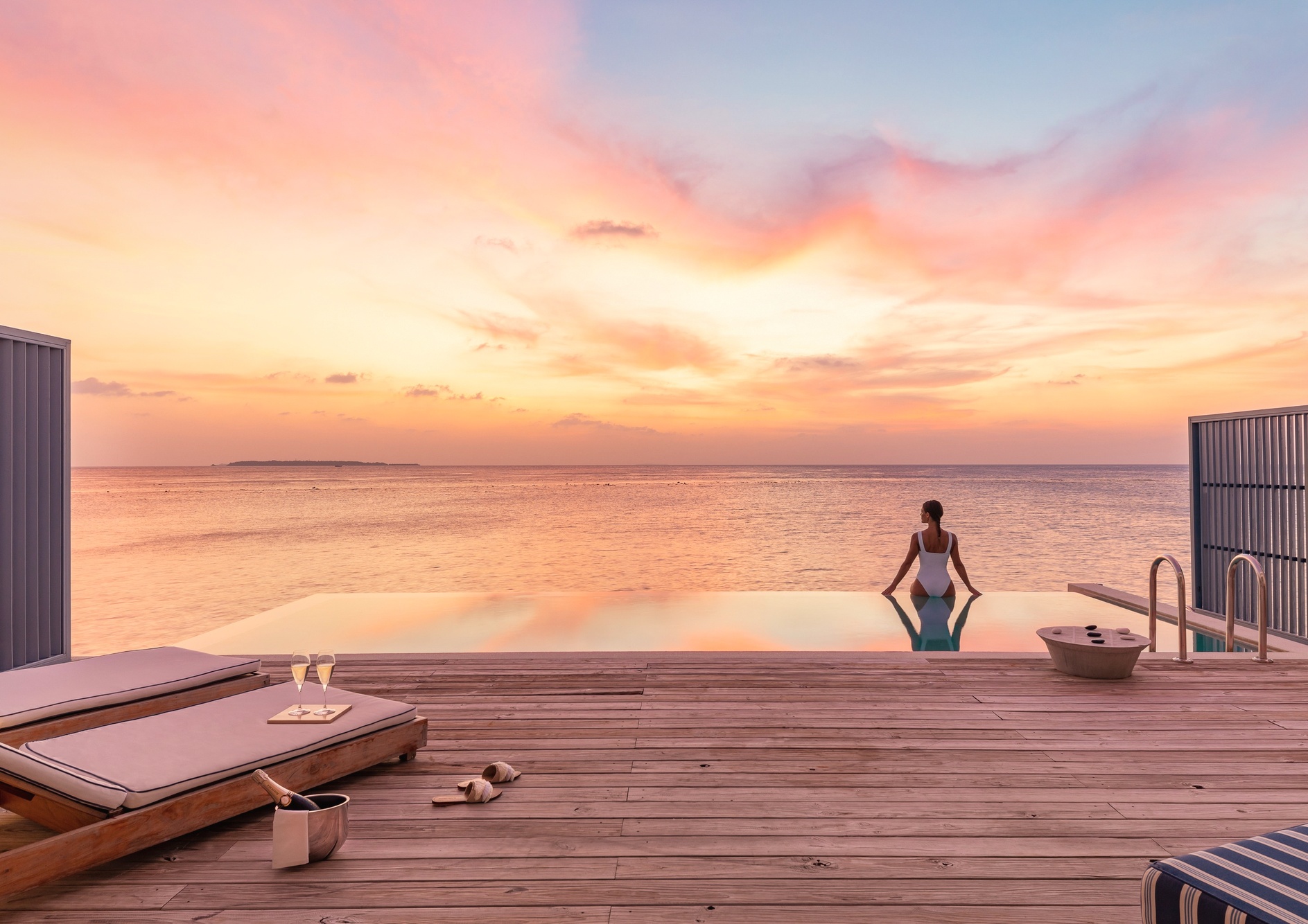 An overwater pool villa at deck level. The pool extends toward open water, the lagoon floor visible beneath.