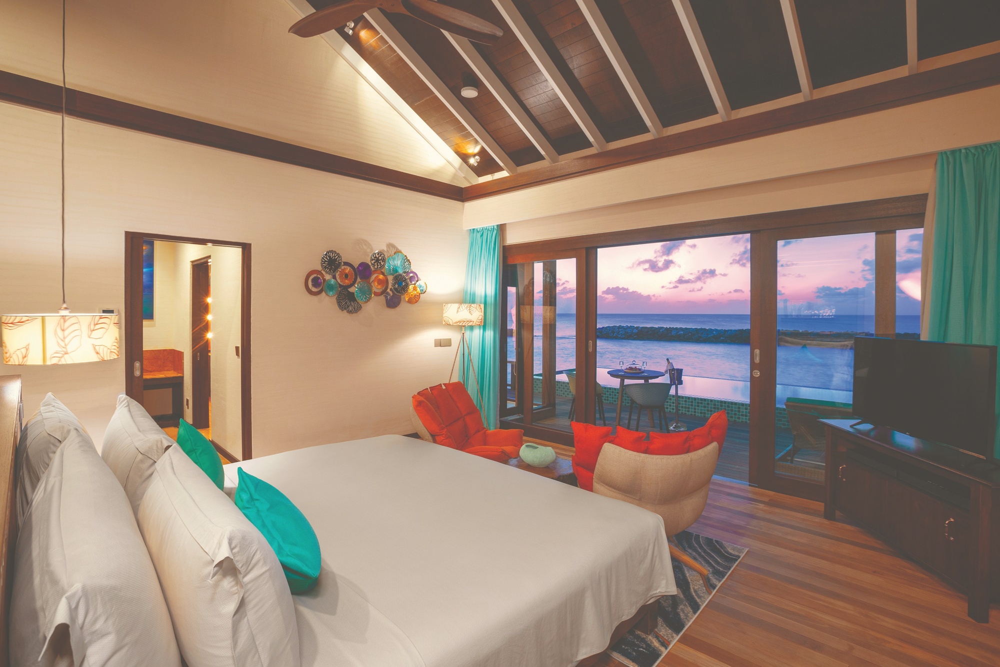 Sunset water villa deck. Atmosphere's overwater proposition, west-facing across the lagoon.