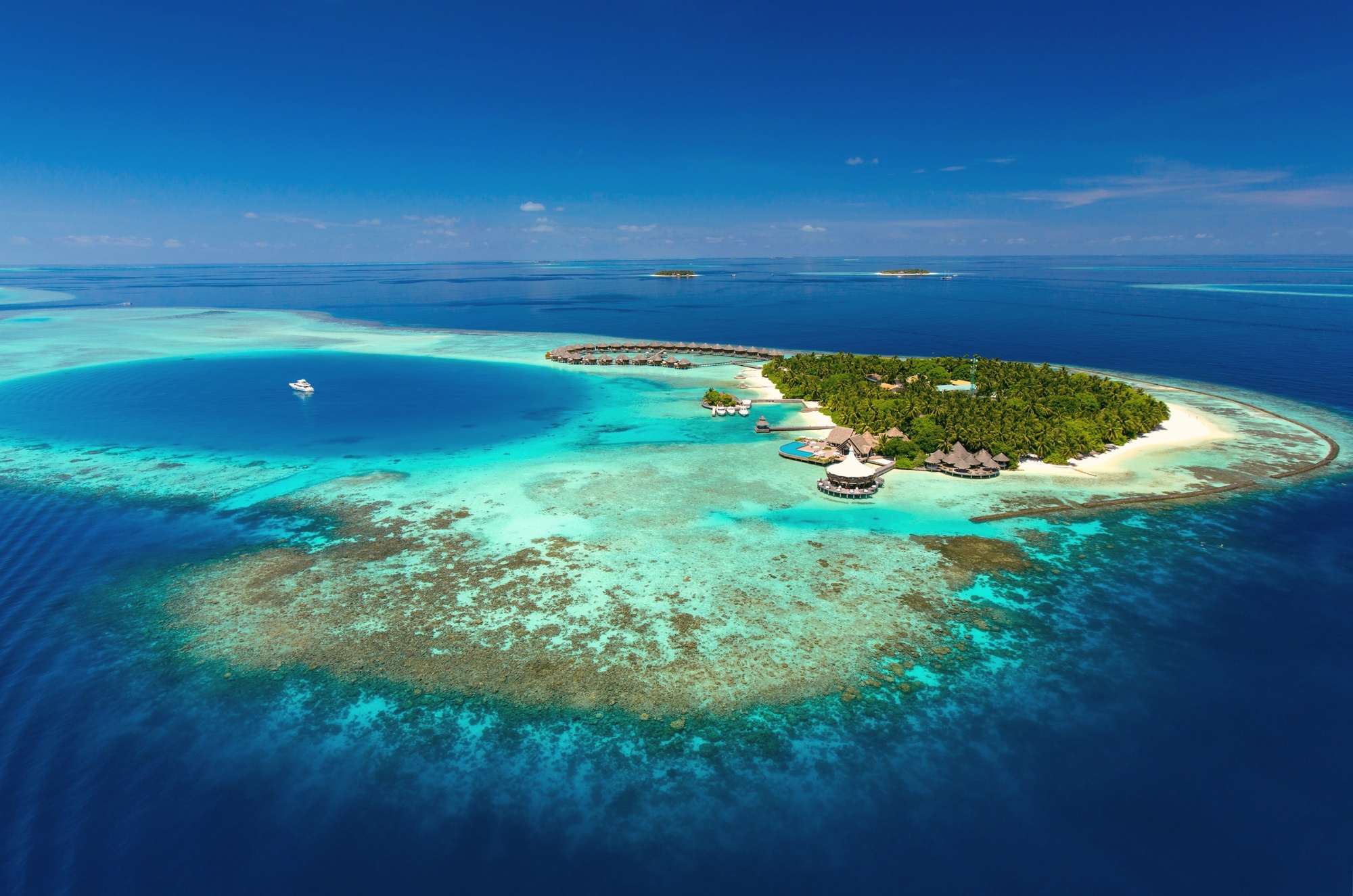 Baros Island from above. The resort occupies its own private island in North Malé Atoll, the villas arranged around the island's perimeter with the lagoon visible on all sides.