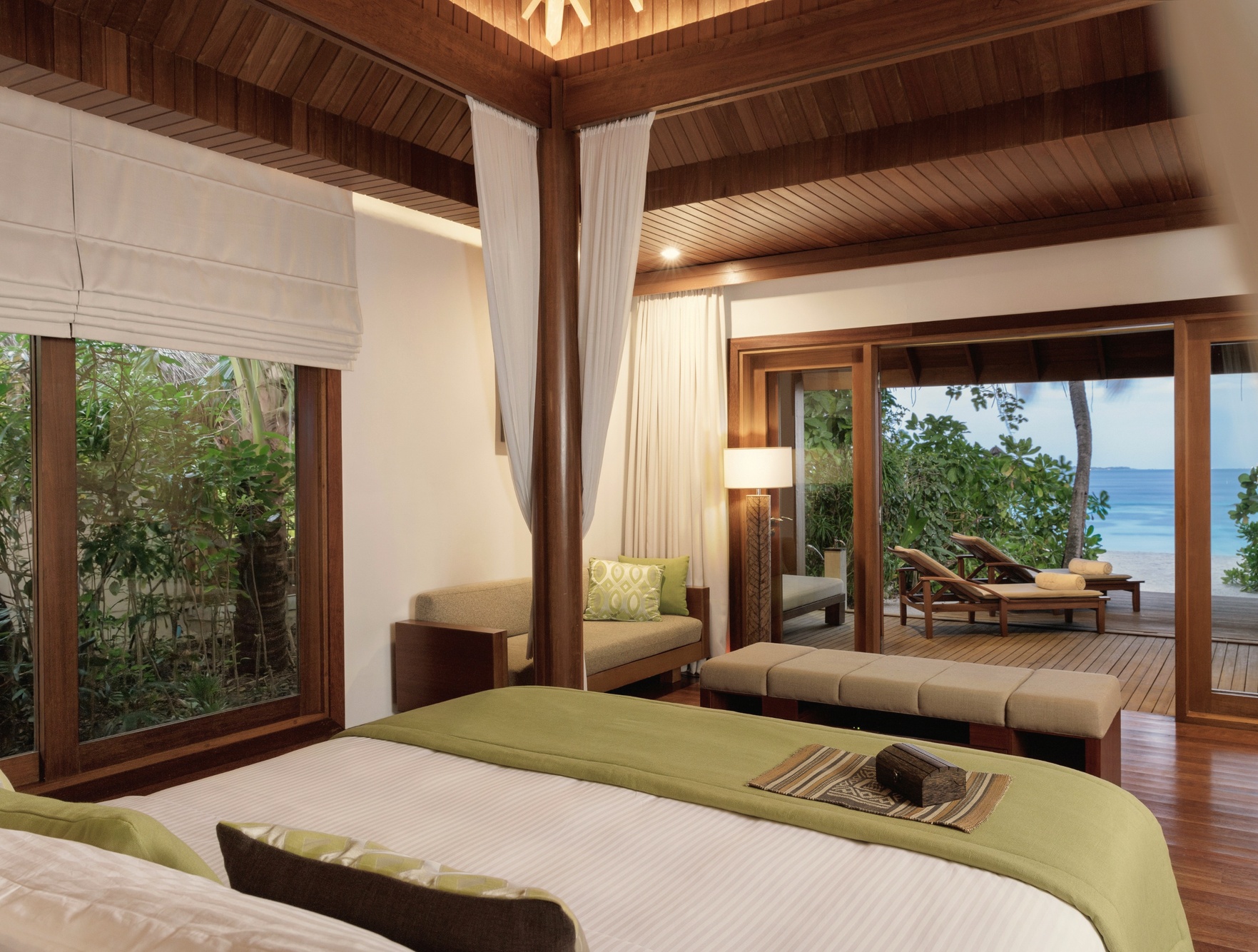 The interior of a Baros Villa. Maldivian-influenced finishes, open-plan layout, and a direct view across the water from the bedroom.