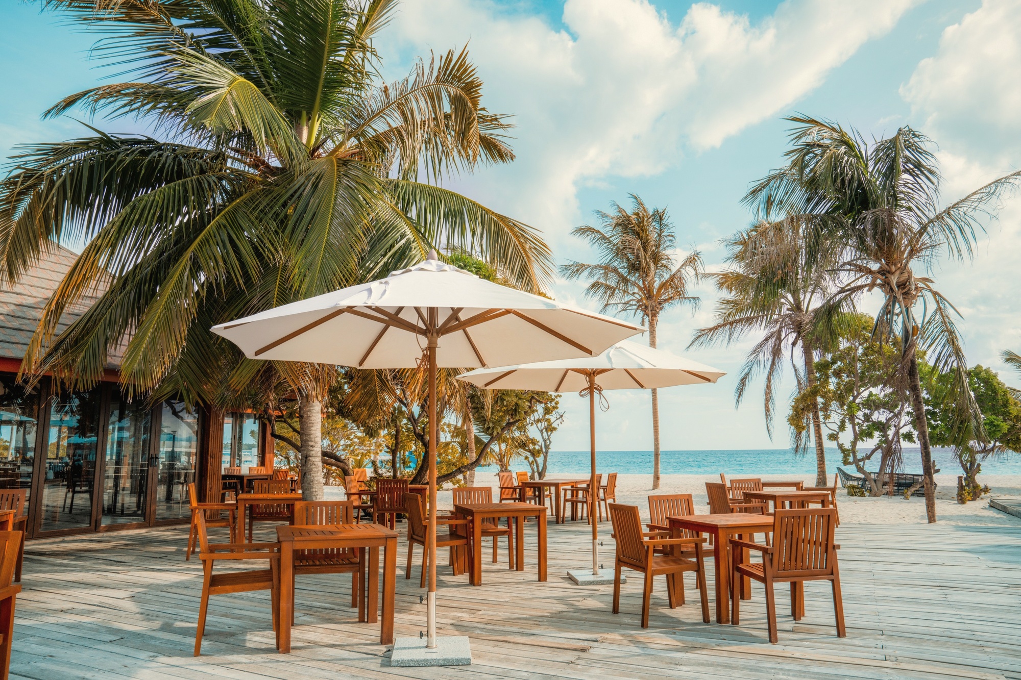 The main dining terrace at dusk. Tables set for dinner with the lagoon as the backdrop and the last light still on the water.