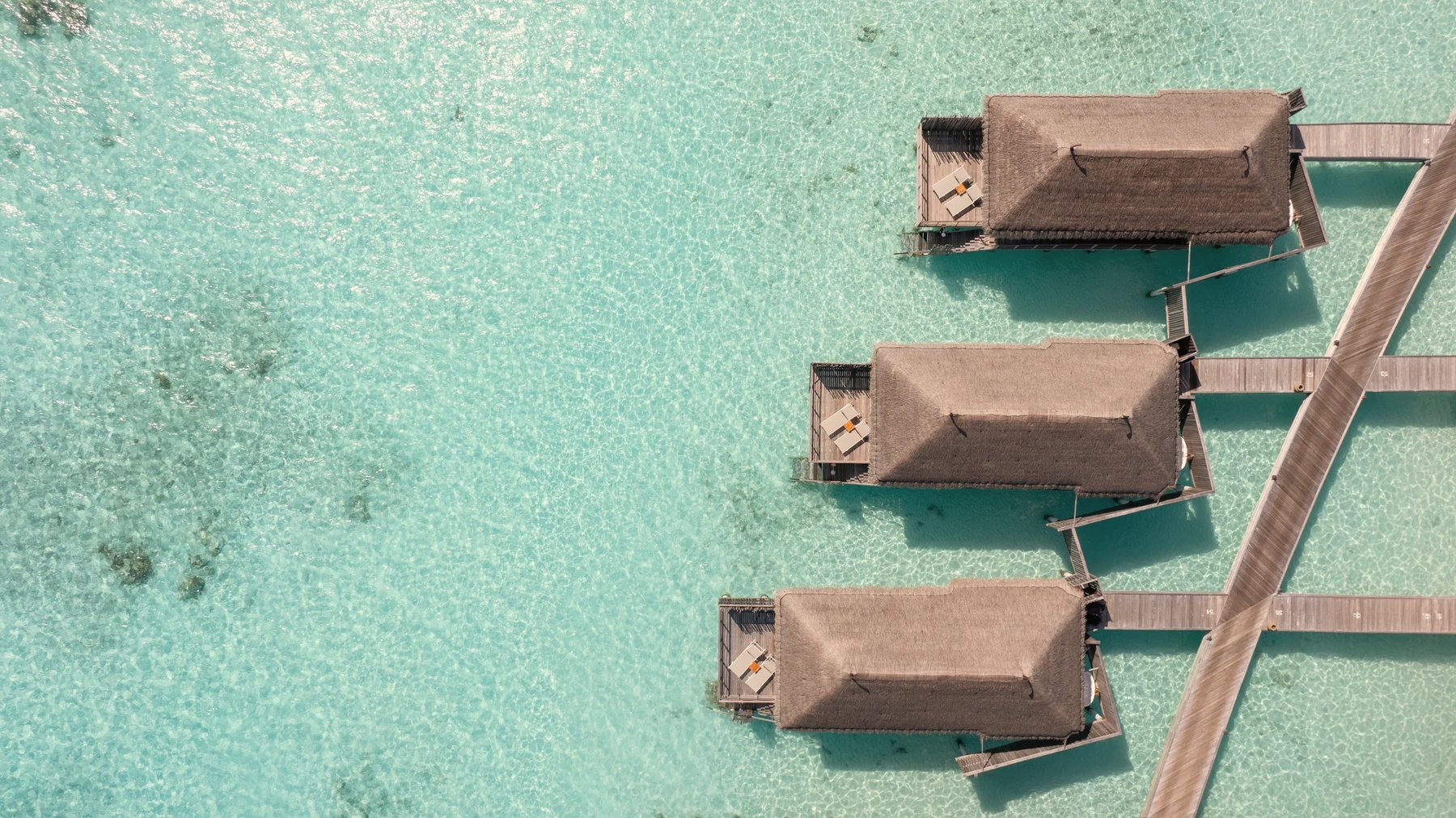An overwater villa deck at water level. The lagoon floor is visible below, and the South Ari horizon is unobstructed.