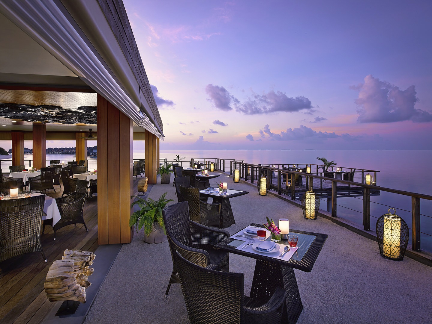 The main dining terrace at dusk. Thai and Maldivian menus are served across multiple venues, with the open-air setting facing the lagoon.