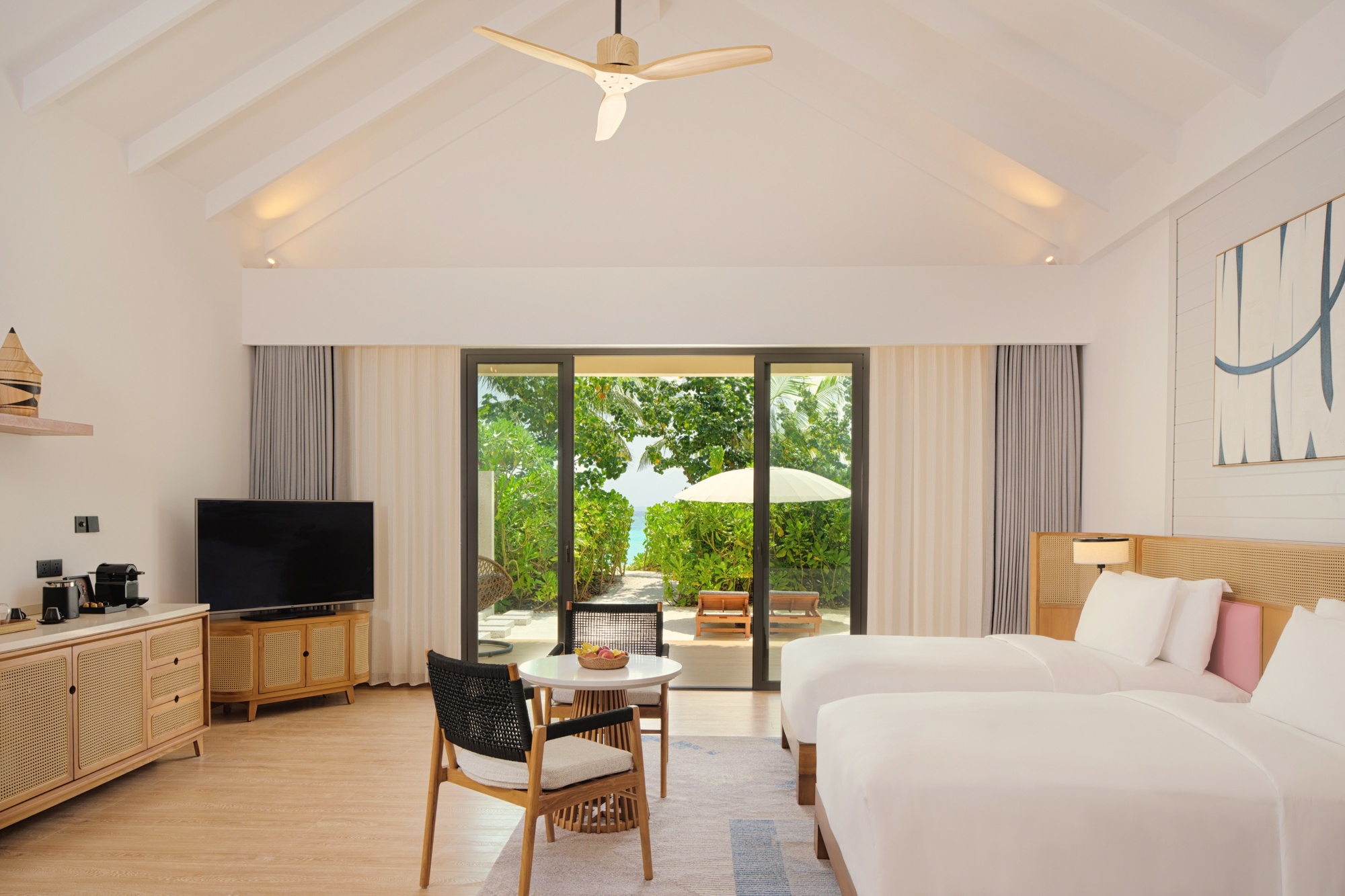 A beach villa interior showing the Thai-heritage design language. Carved timber details and warm tones distinguish the rooms from the standard Maldives palette.