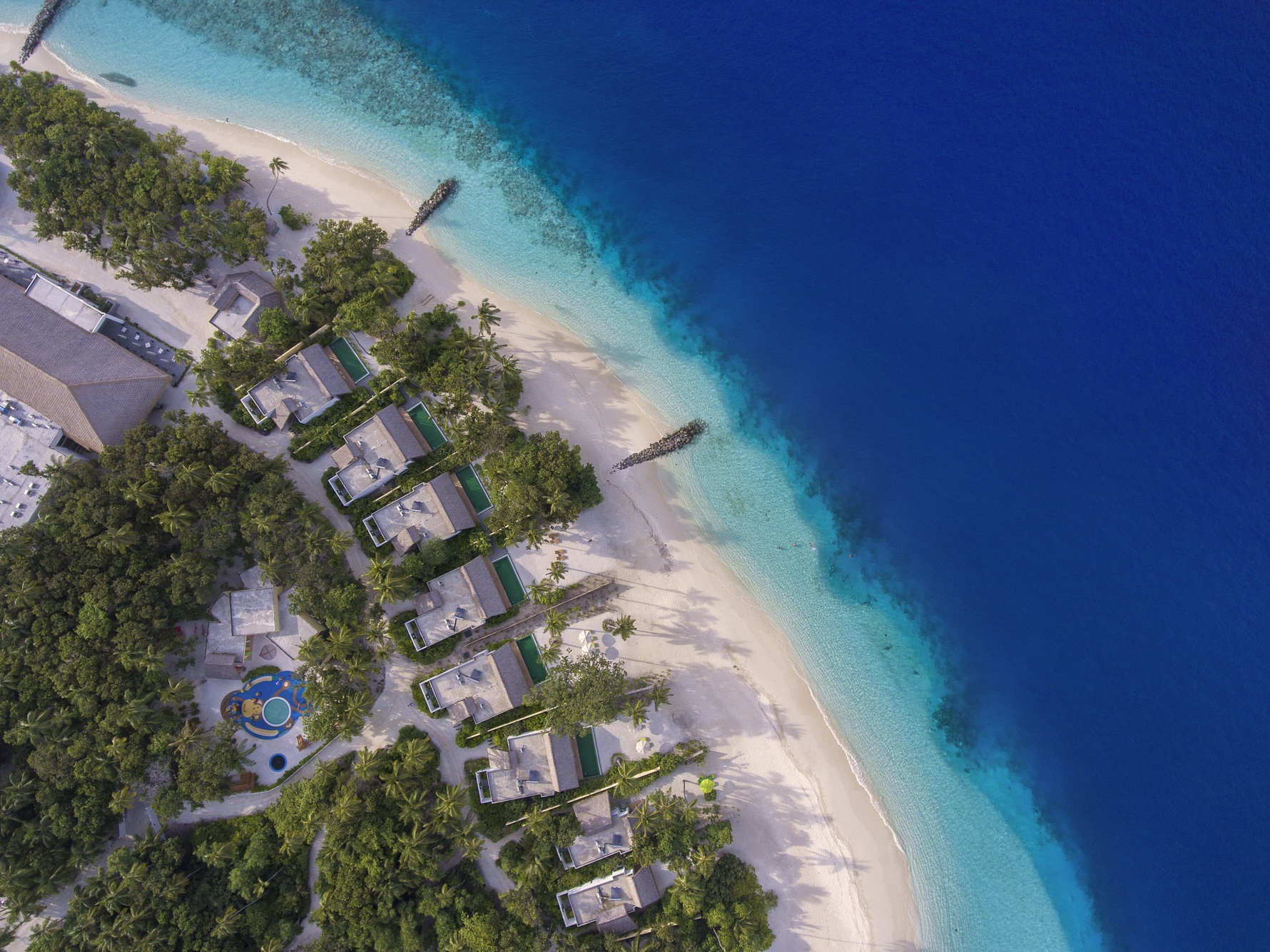 Fasmendhoo Island from above, the resort's overwater villa jetties extending into the Raa Atoll lagoon.