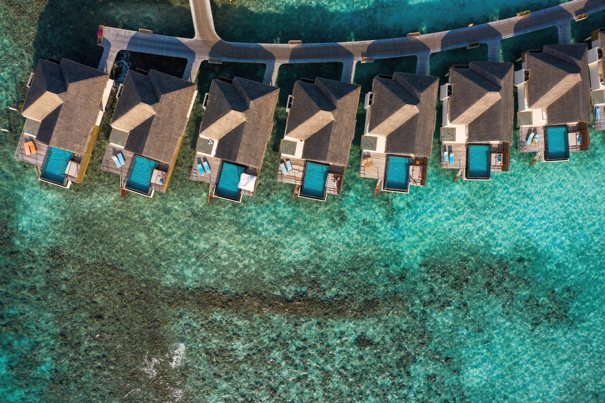 An overwater pool villa at the lagoon edge. The deck extends directly above the water, with the pool positioned to face the open ocean.