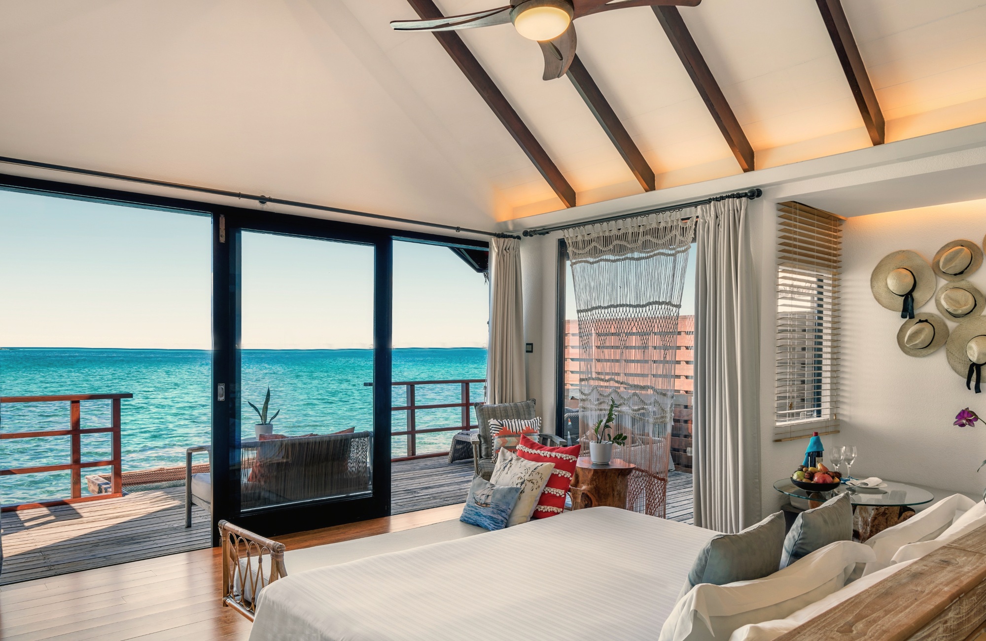 The interior of an overwater villa. Clean lines, lagoon-facing glazing, and a private pool visible through the sliding doors.