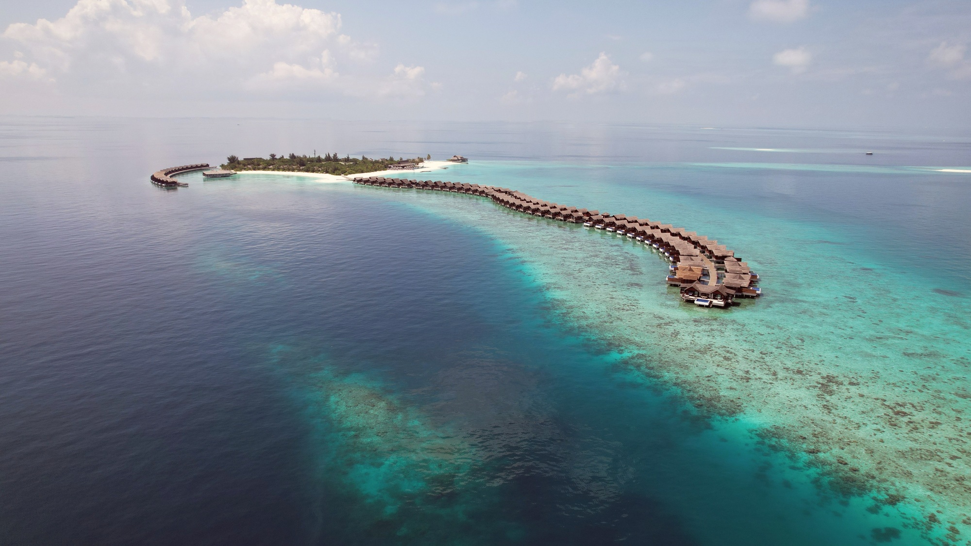 Kodhipparu from above. A compact coral island in North Malé Atoll, the overwater villa jetties extending out over the lagoon on both sides of the island.