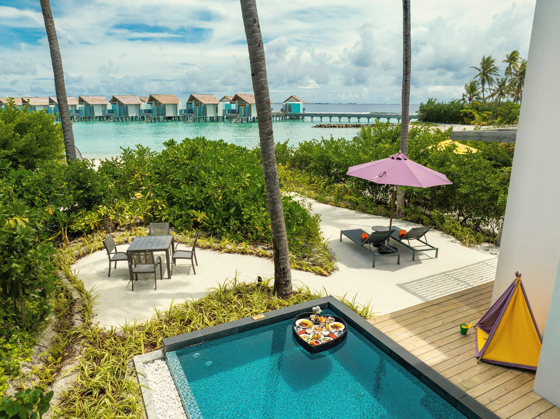 A beach villa exterior looking toward the lagoon. The villa categories step from hotel-style rooms through to pool villas at the beach edge.