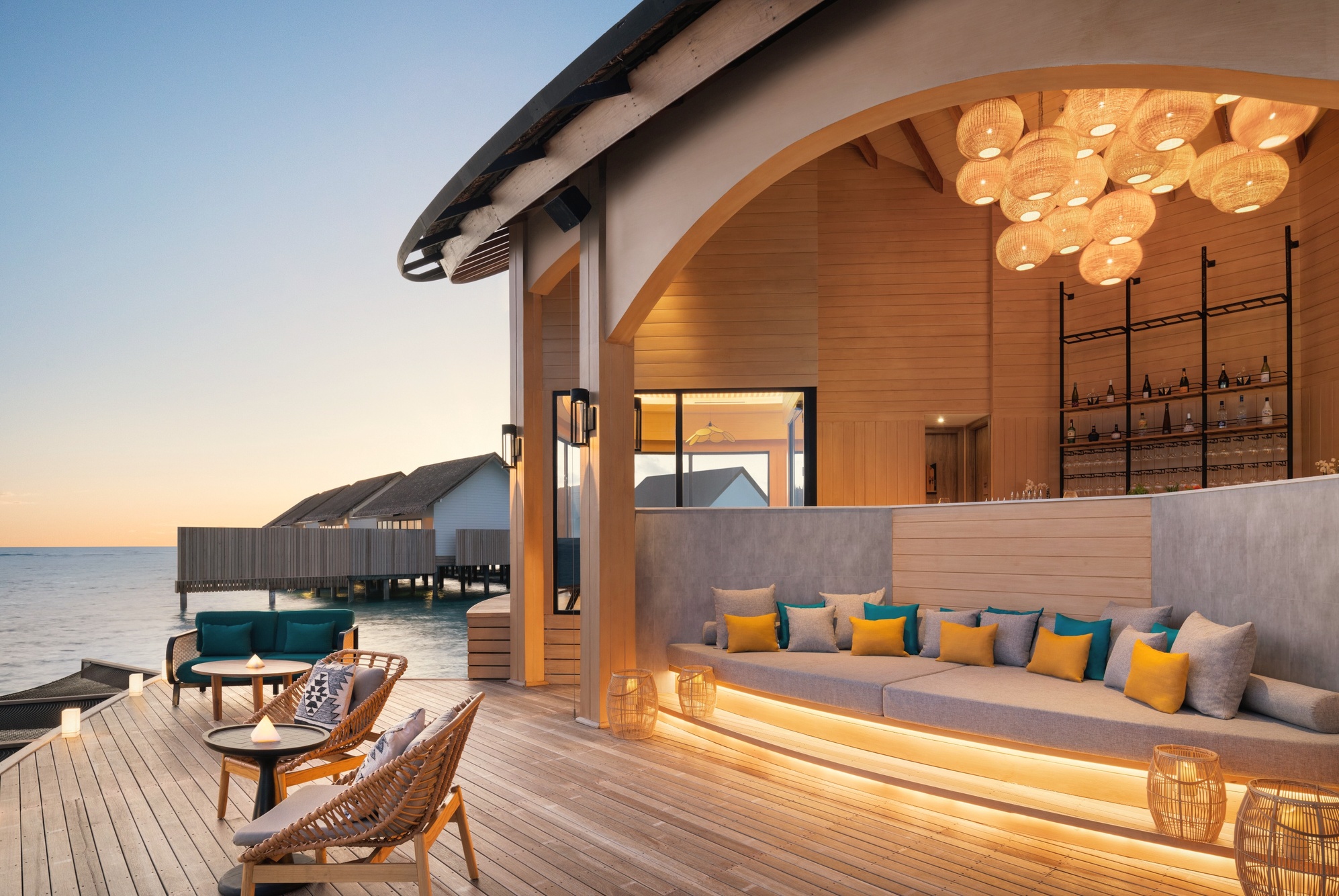 The main dining terrace at dusk. Tables set above the water, the North Malé horizon behind.