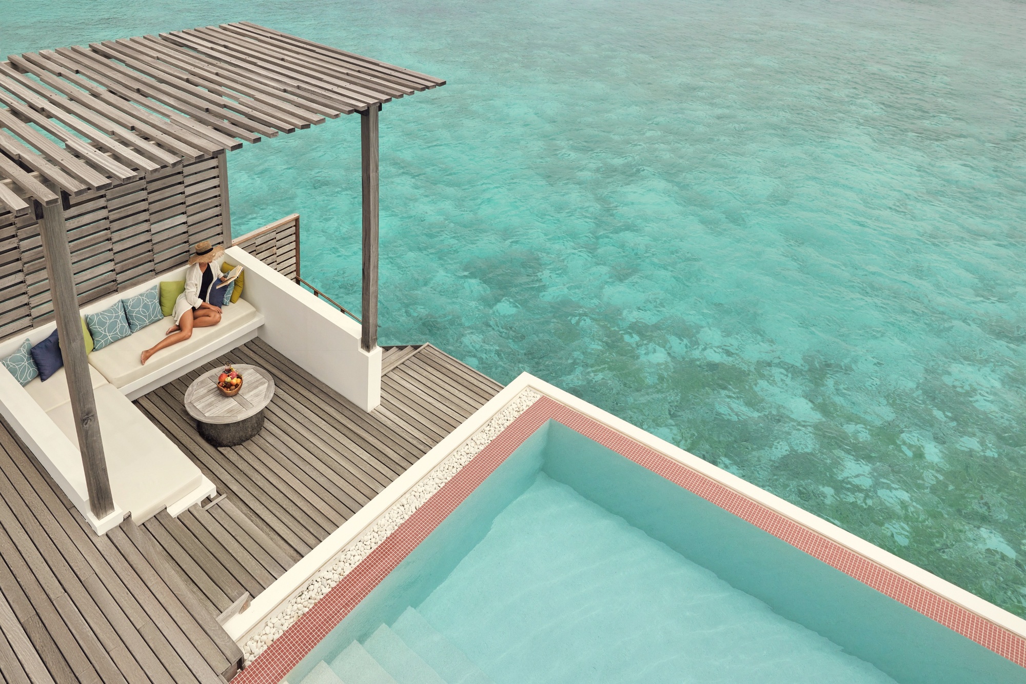 A water villa exterior at dusk. The overwater configuration extends directly above the lagoon, with pool deck and direct water access.