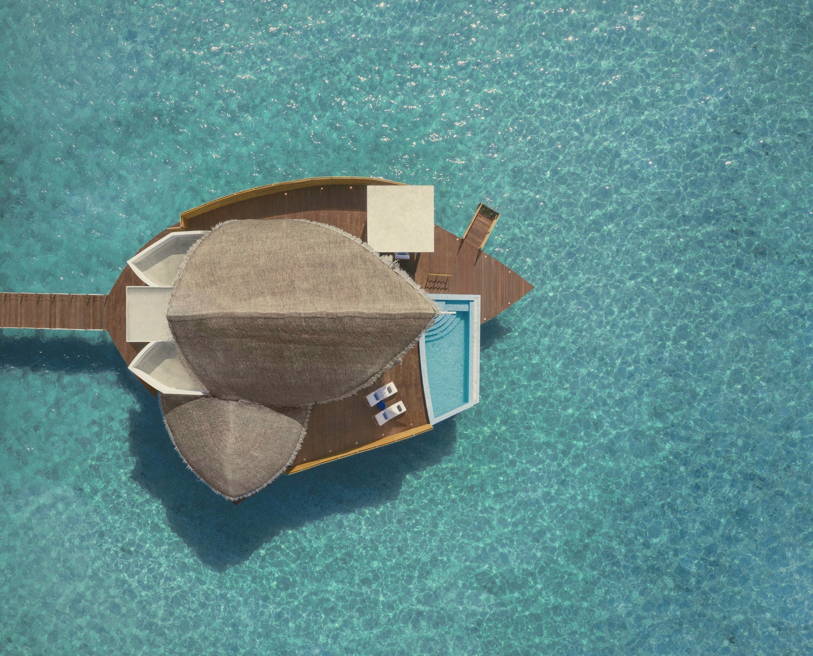 An overwater pool villa at dusk. The deck extends directly over the water, with a private pool and unobstructed views across the atoll.