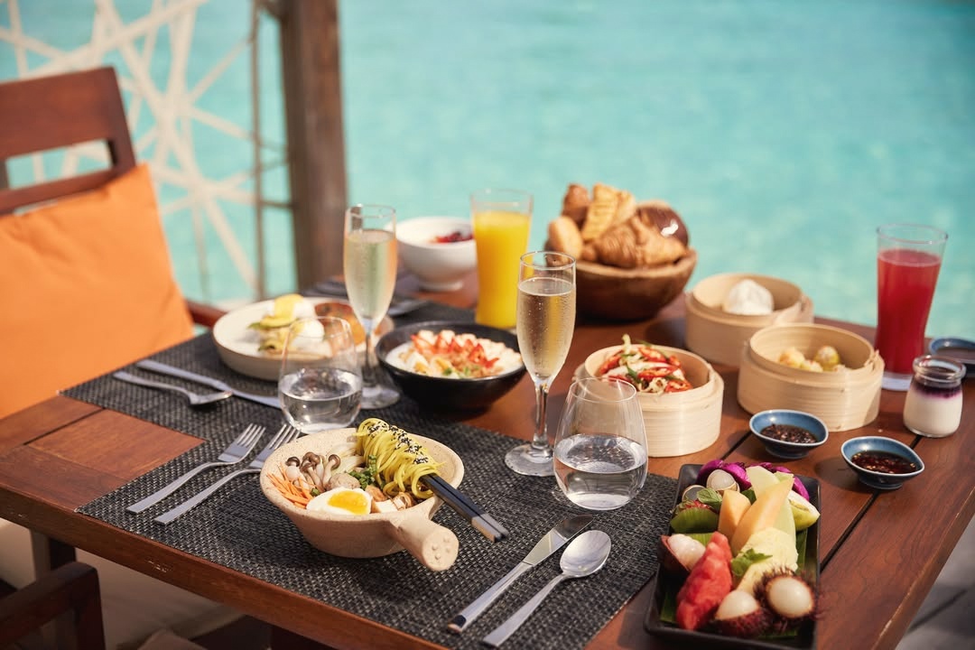 Dining at the water's edge. The main restaurant at LUX* South Ari Atoll opens onto the lagoon, with tables positioned to face the horizon at sunset.