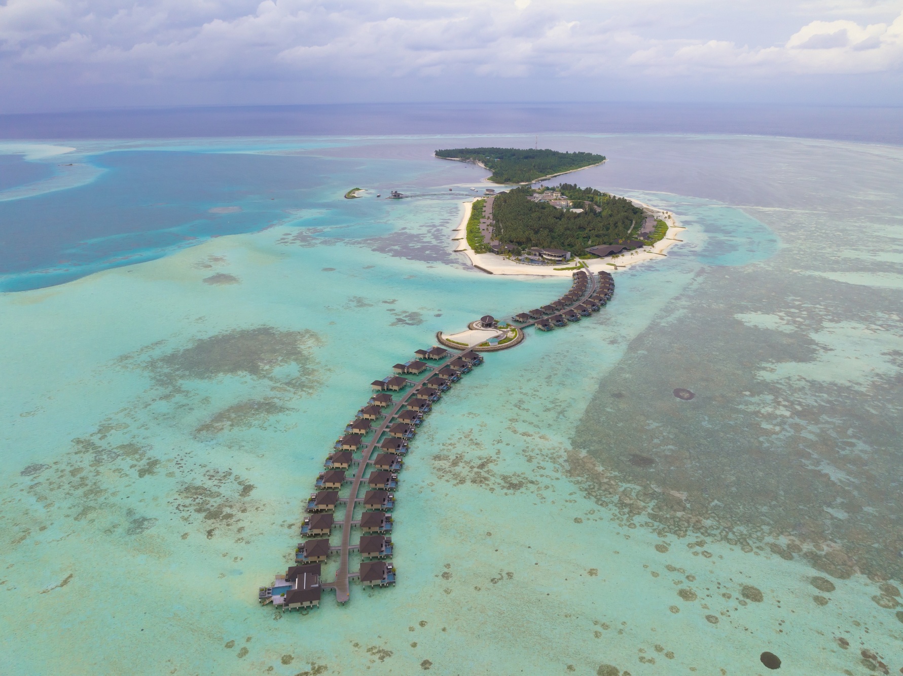 Madifushi from above. The private island sits in Meemu Atoll, its lagoon visible on all sides and the villa footprint modest against the surrounding water.