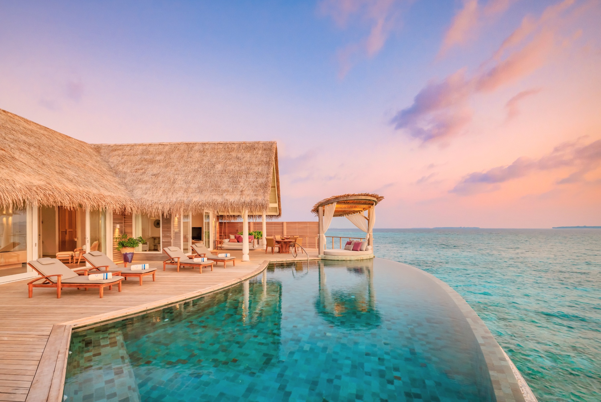 An overwater villa at deck level. The lagoon below is clear and shallow, with the house reef visible from the villa edge.