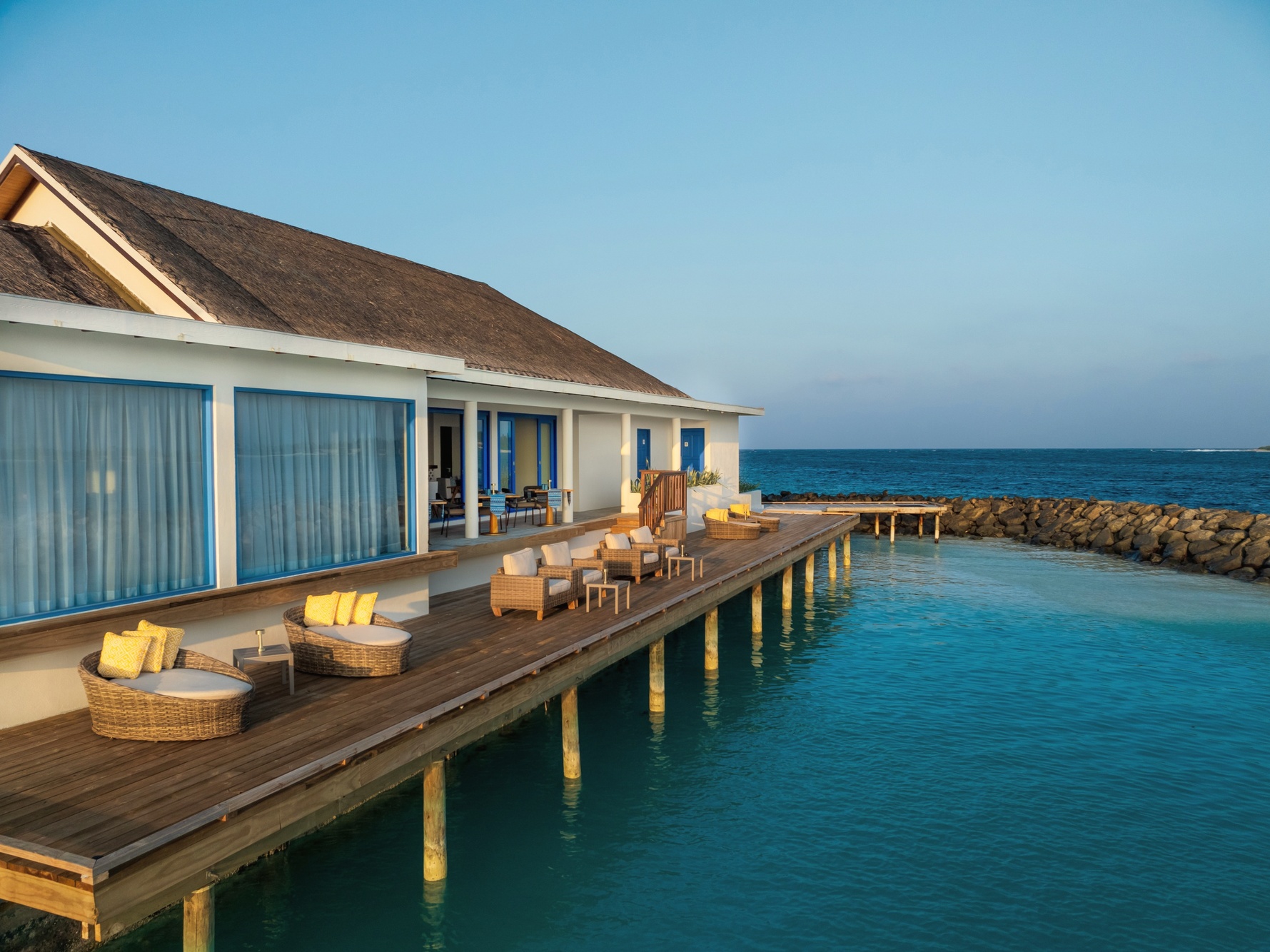 The all-inclusive dining room at dusk. Tables set for the evening service, the water visible on three sides.