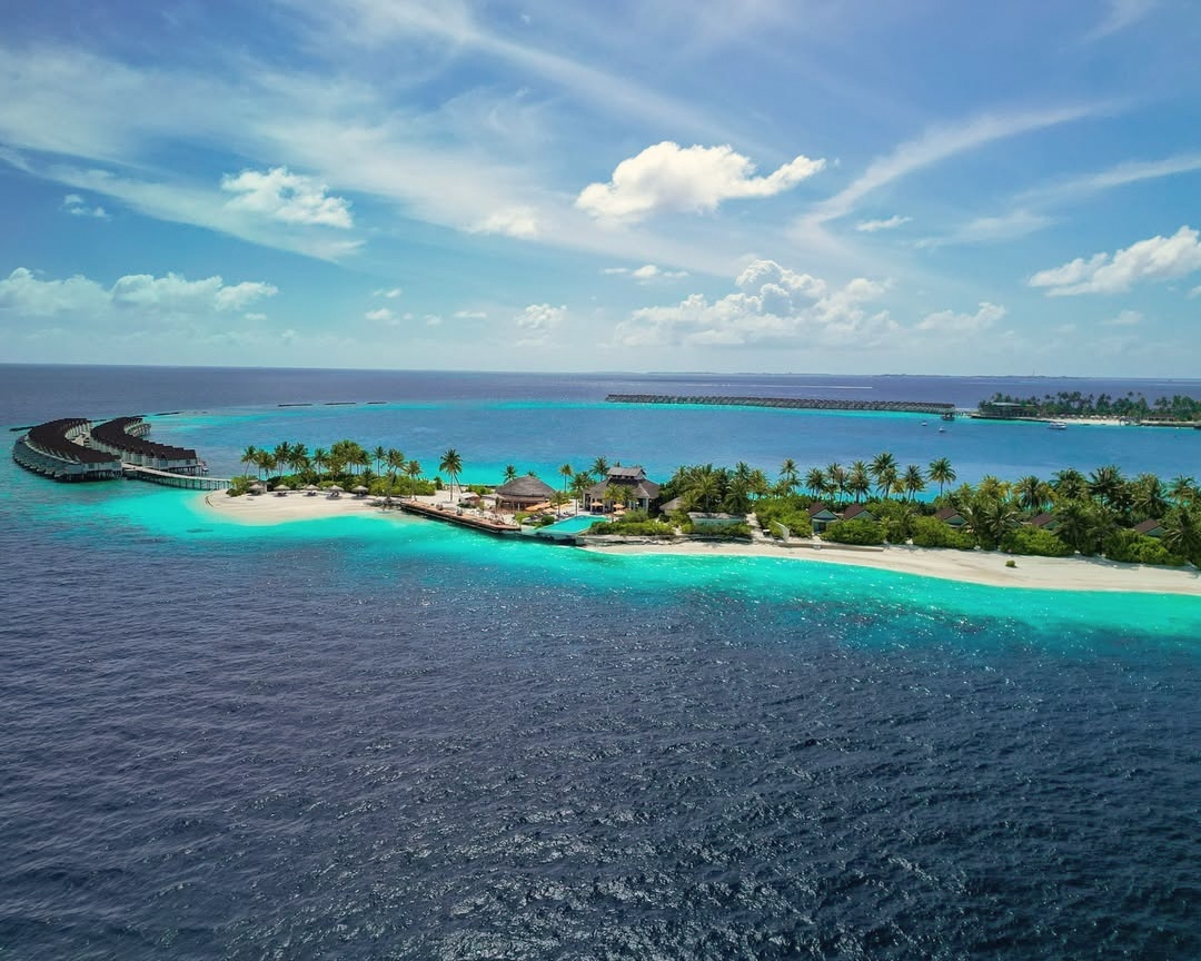 Lobigili from above. A small private island in North Malé Atoll, the overwater villa jetties extending into the lagoon on both sides.