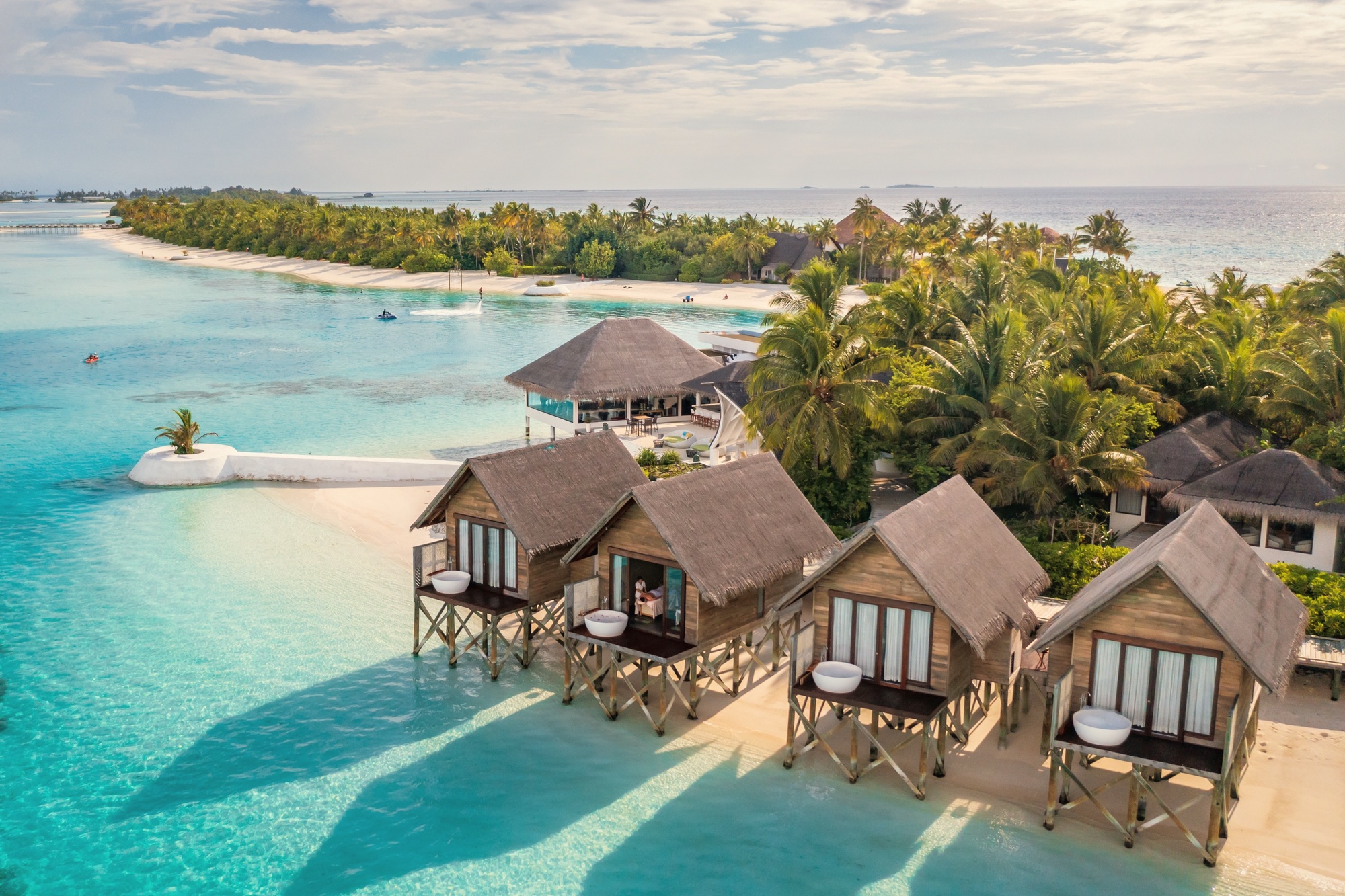 Maadhoo from above. The island sits in South Malé Atoll, the resort's 107 villas arranged across beach and overwater positions with the lagoon visible on both sides.