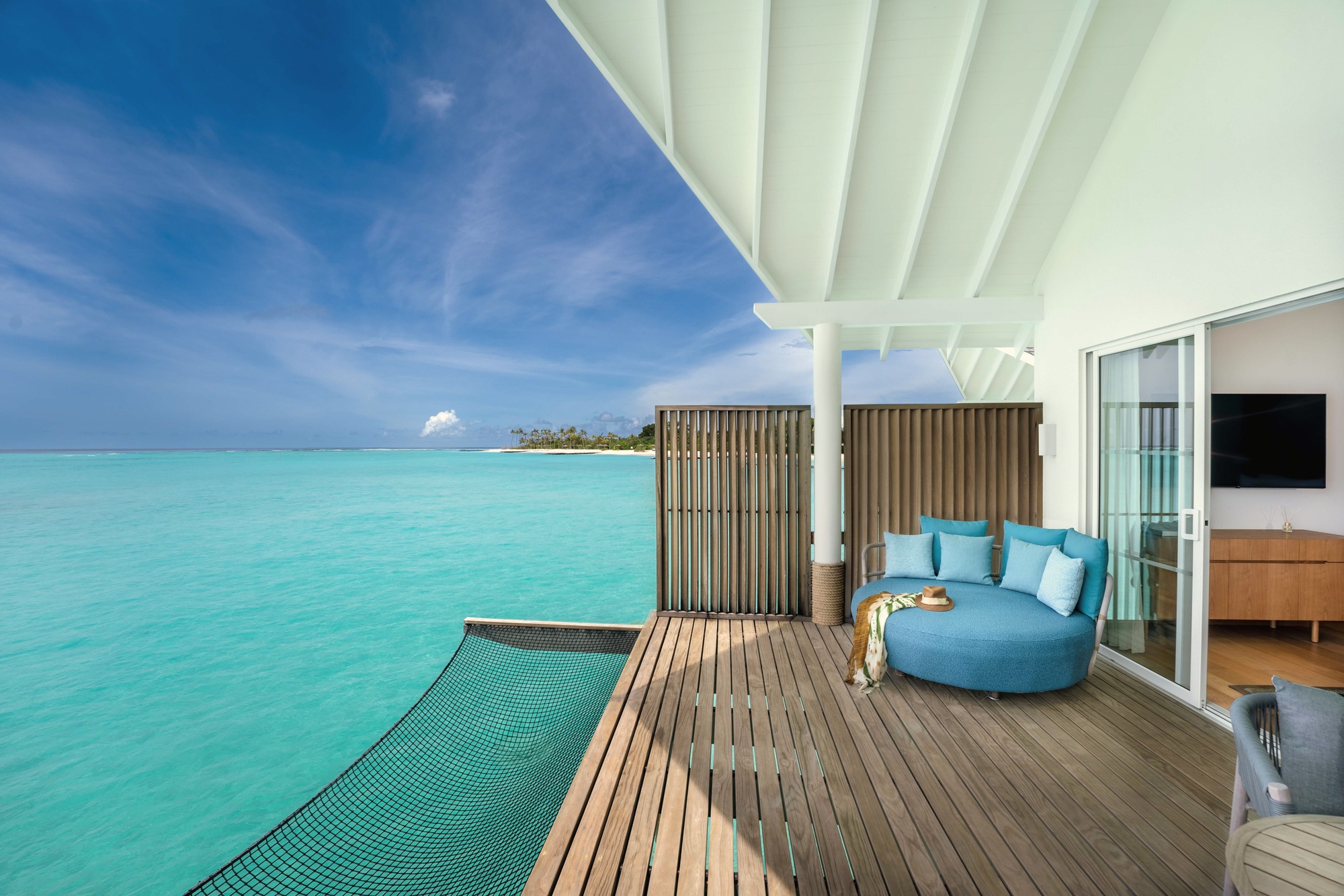 An overwater villa exterior at dusk. The deck extends directly above the lagoon, with the water colour shifting from turquoise to deep blue at the reef edge.