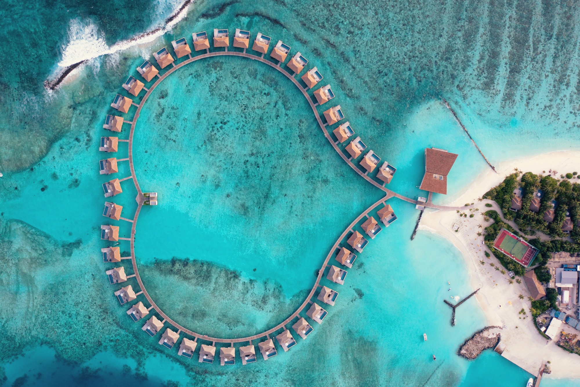 Huruelhi Island from above. The resort sits on its own island in South Ari Atoll, the overwater villa jetties extending into the lagoon from both sides.