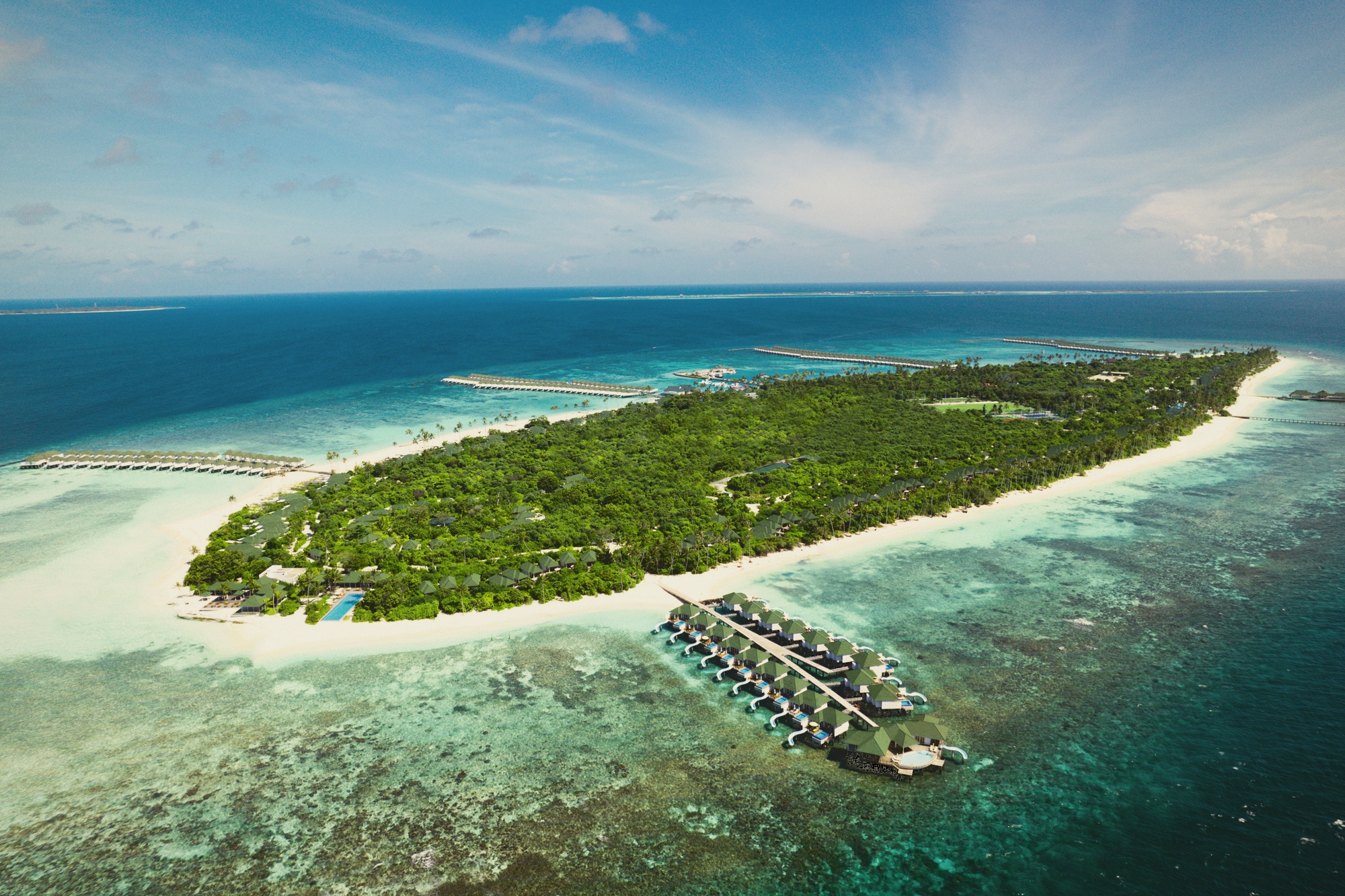 Siyam World from above. The resort occupies its own island in Noonu Atoll, with overwater villa rows extending into the lagoon and the water park visible at the island's edge.
