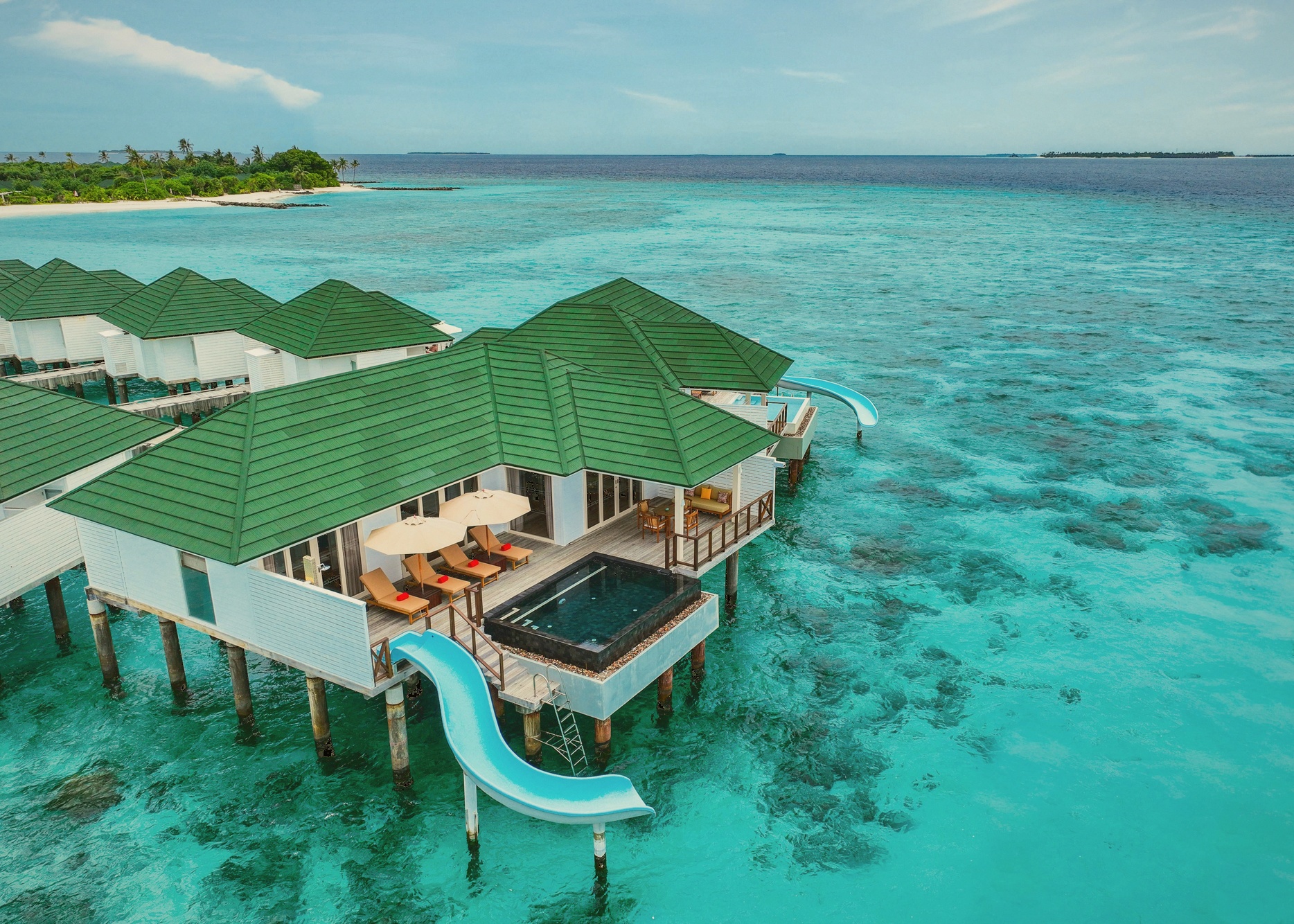 An overwater villa at dusk. The decks extend directly above the lagoon, with the water clear enough to see the reef below.