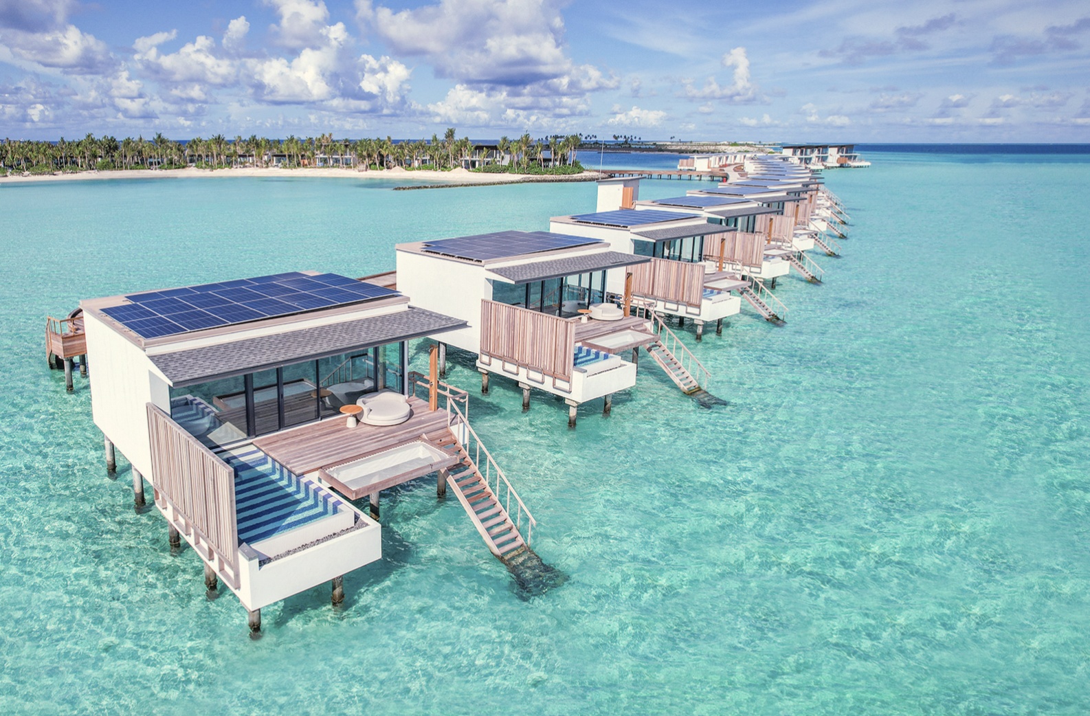 An overwater villa from the deck. The water-pool edge opens directly onto the lagoon, with the horizon unobstructed.