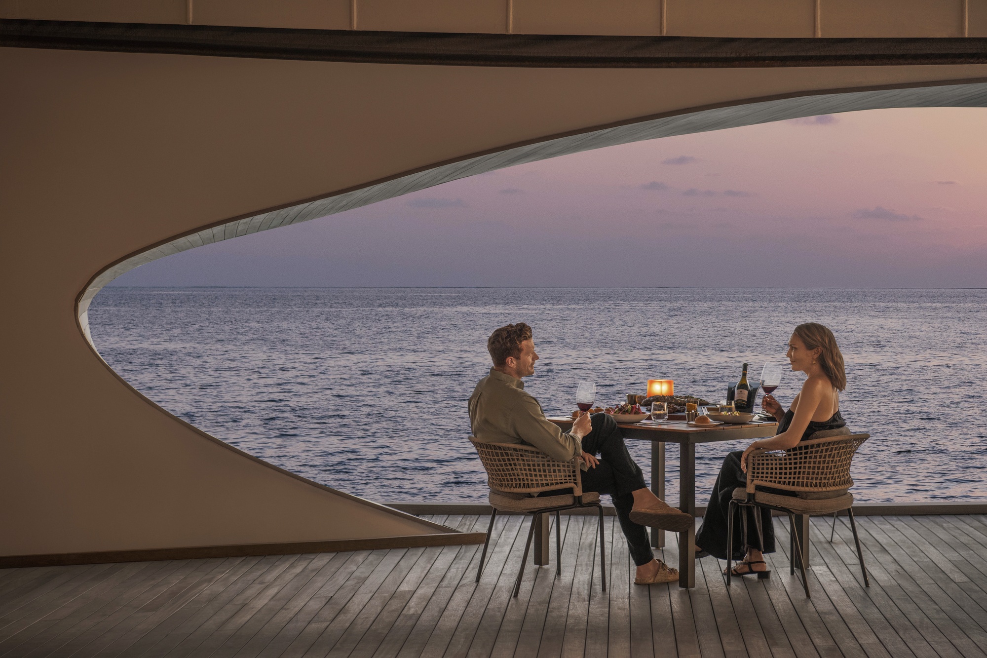 The overwater restaurant at dusk. The dining programme spans multiple venues, with the overwater setting the most photographed.