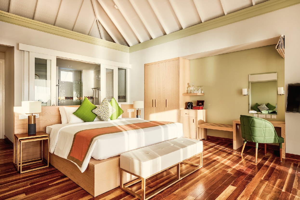 The interior of a Grand Water Villa. The room opens toward the water on the lagoon-facing side, with the South Malé light coming in low across the floor.