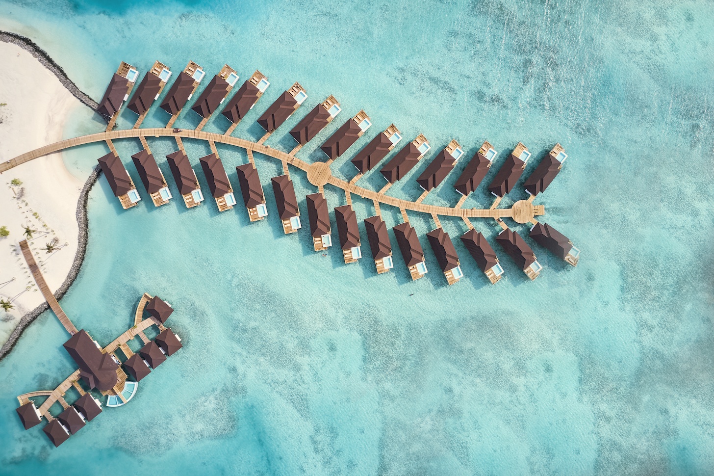 Olhuveli from above. The resort occupies its own island in South Malé Atoll, with overwater villa jetties extending across the lagoon on both sides.
