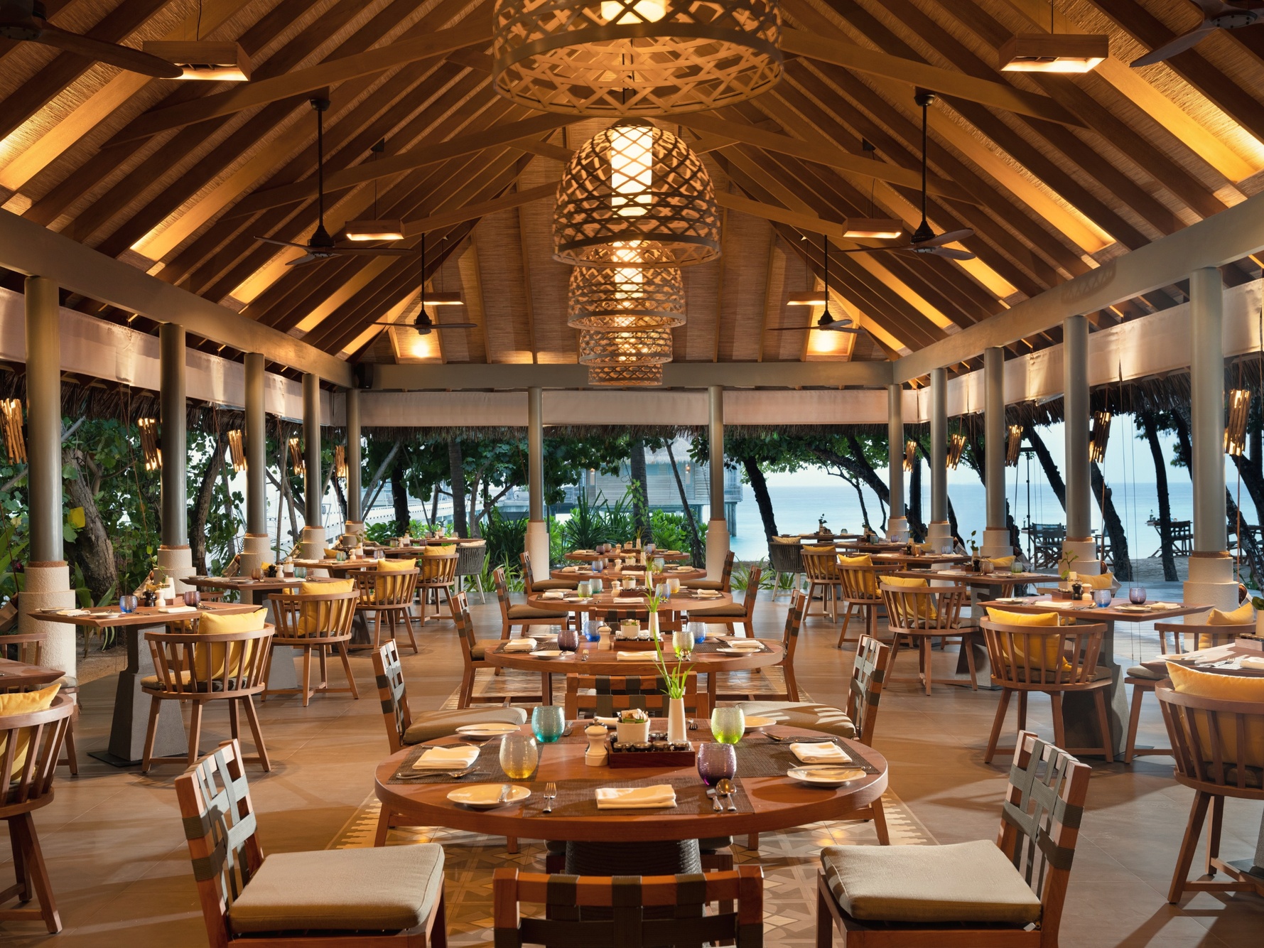 Dining at the overwater restaurant. Tables set above the lagoon at the edge of the reef, with the atoll visible in the distance.